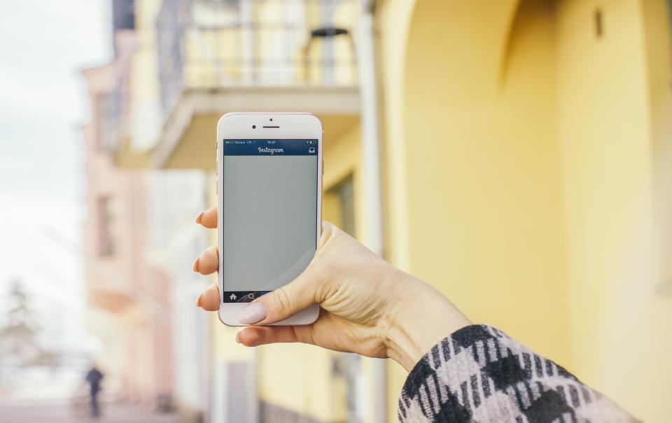 Mão segurando um celular com o aplicativo do Instagram aberto em uma rua